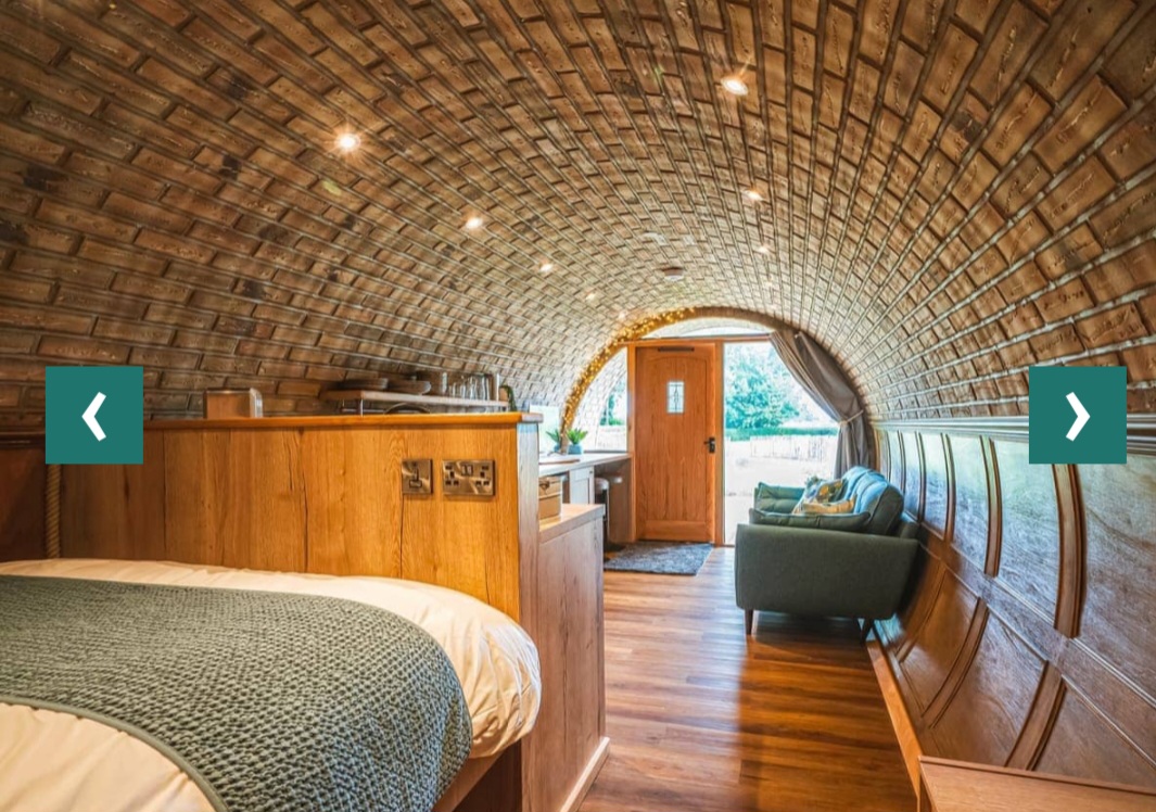 Inside the Ayrshire 8M Burrow — the brick-arched barrel ceiling, King-sized bed on the left, green armchair, kitchen counter and door to the pasture